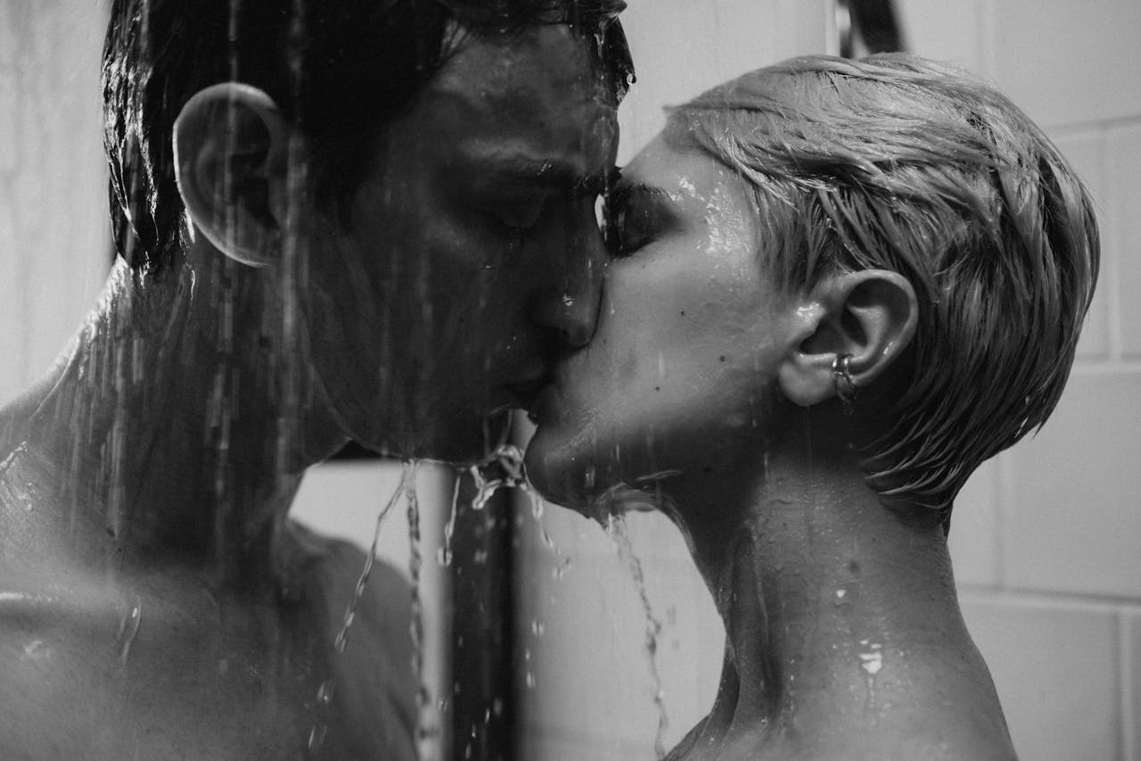 Home Intimate grayscale image capturing a couple kissing passionately in a shower.