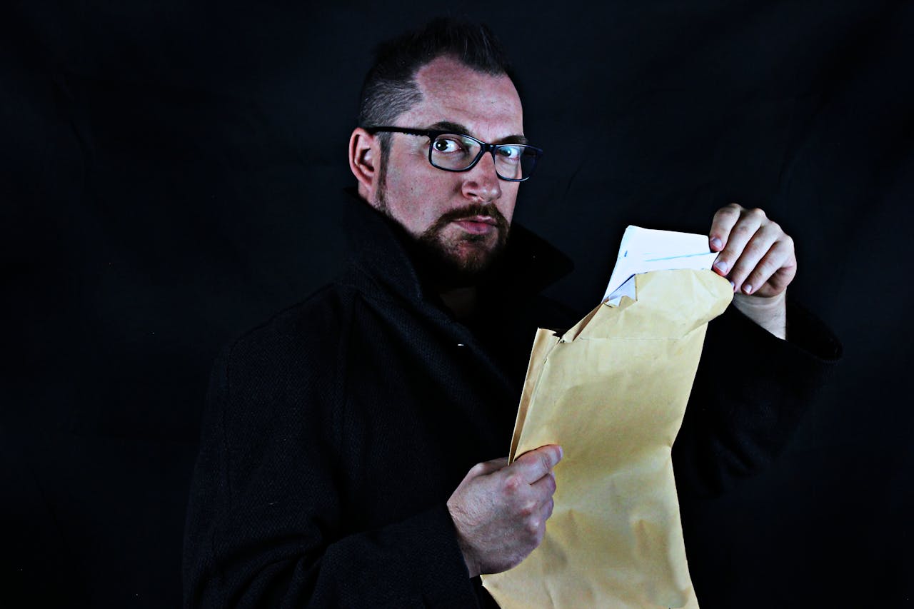 Home Portrait of a man with eyeglasses opening a brown envelope, dark background.